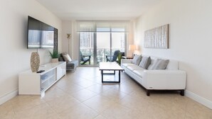 A spacious living room with a white sofa, a coffee table, and a TV mounted on the wall. - Ocean Reserve (Sunny Isles Beach)
