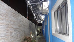 Un pasillo estrecho con una pared azul y una pared de ladrillo blanco en un lateral. Hay plantas en macetas a lo largo del pasillo.