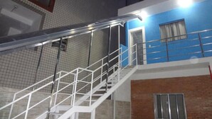 Una escalera con barandillas metálicas que conduce a un edificio con pared exterior azul y una ventana con cortinas.