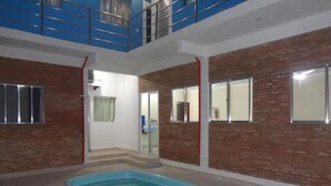 Una piscina interior con suelo de baldosas azules, rodeada de paredes de ladrillo y una puerta de cristal que da a un balcón.