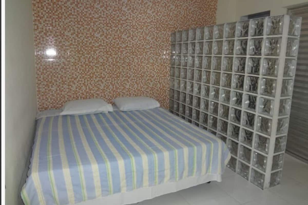 A bedroom with a striped bedspread, a tiled wall, and a glass block partition.
