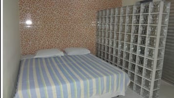Quarto com colcha listrada, parede azulejada e divisória de vidro.