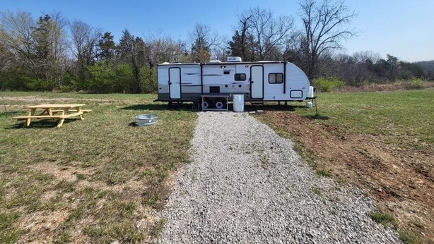 A recreational vehicle parked in a grassy area with a gravel path leading to it. - The Budget Suite (Leadwood)