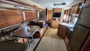 A compact RV interior with a kitchenette, a dining area, and a seating area with a sofa and table. - The Budget Suite (Leadwood)