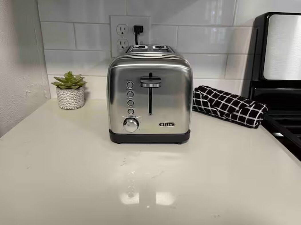 A kitchen with a silver toaster on a white countertop, a small potted plant, and a black and white checkered cloth.