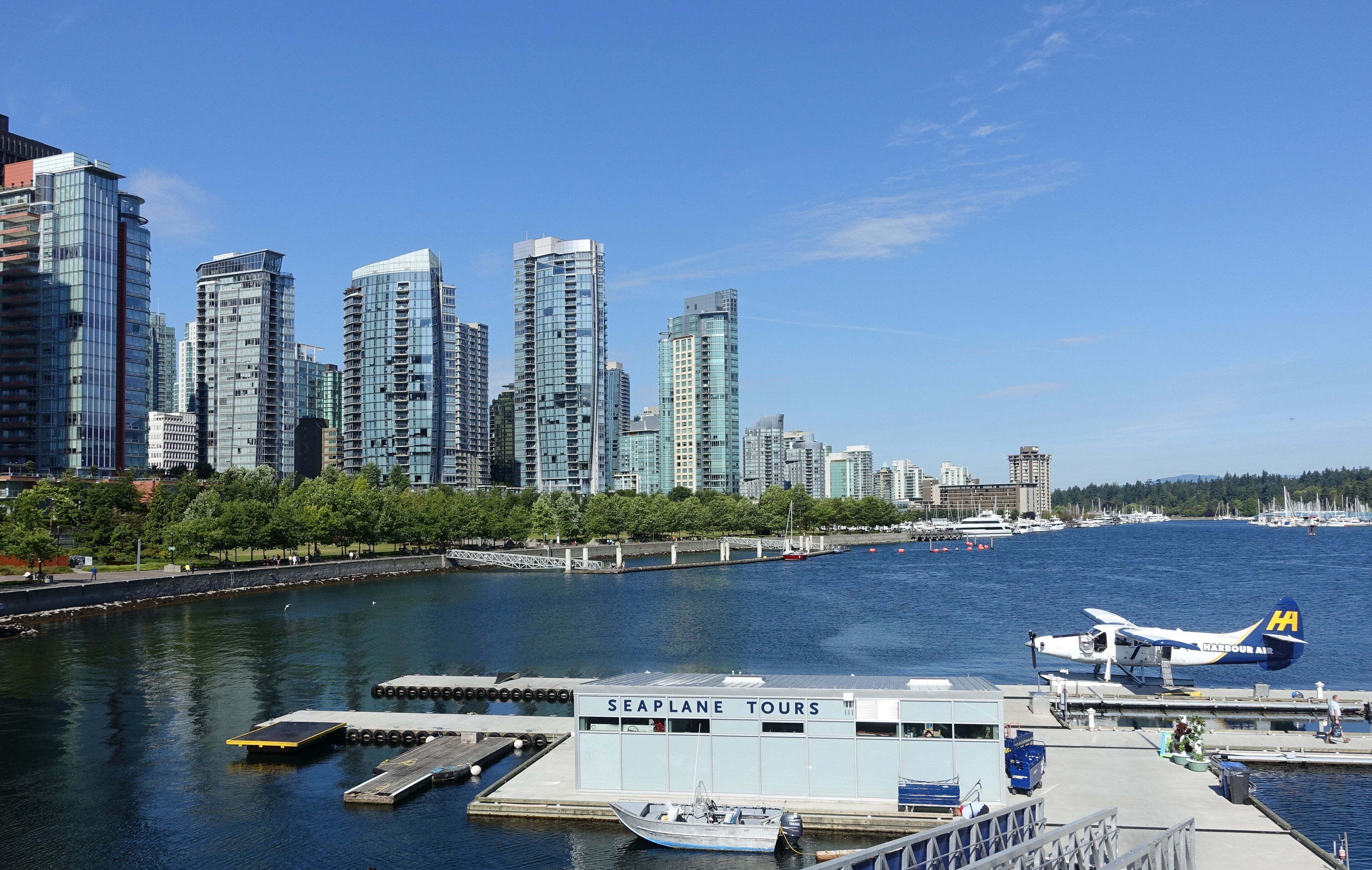 Une vue sur la ville, avec ses bâtiments modernes et imposants qui bordent le front de mer, un quai où est amarré un hydravion, et une enseigne indiquant les circuits touristiques en hydravion.