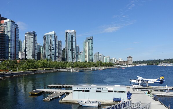 Paisaje urbano frente al agua con modernos rascacielos, un muelle y un hidroavión, y un cartel de Excursiones en Hidroavión.