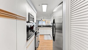 A narrow kitchen with white cabinets, a stainless steel refrigerator, and a wooden countertop. - Oceanfront Oasis. Expansive balcony, cozy decor, stunning views over the dunes. (Fort Walton Beach)
