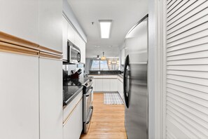 Une cuisine étroite avec des meubles blancs, un réfrigérateur en acier inoxydable et un plan de travail en bois.