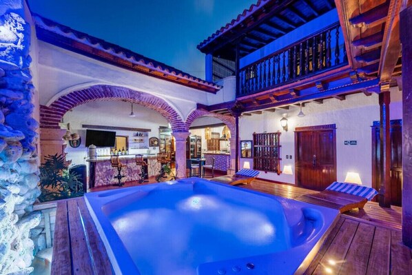 A pool area with a hot tub, wooden deck, and a bar area.