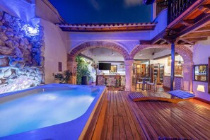 A pool area with a stone wall, wooden deck, and a bar area with seating. - Casa De La Moneda, Walled city 6BD (Cartagena de Indias)