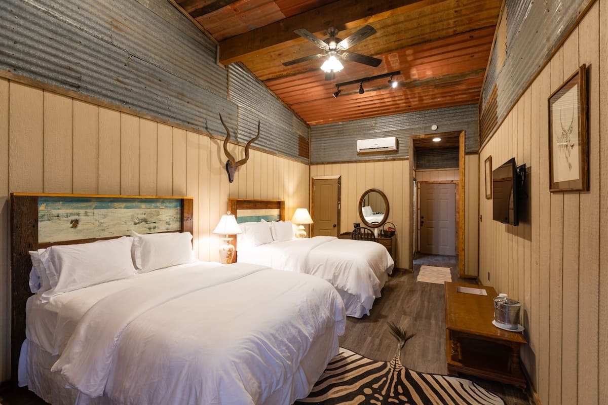 Quarto com duas camas, teto de madeira e ventoinha.
