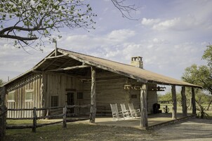Een houten gebouw in rustieke stijl met een veranda en overdekt terras, omringd door bomen en een heldere lucht.