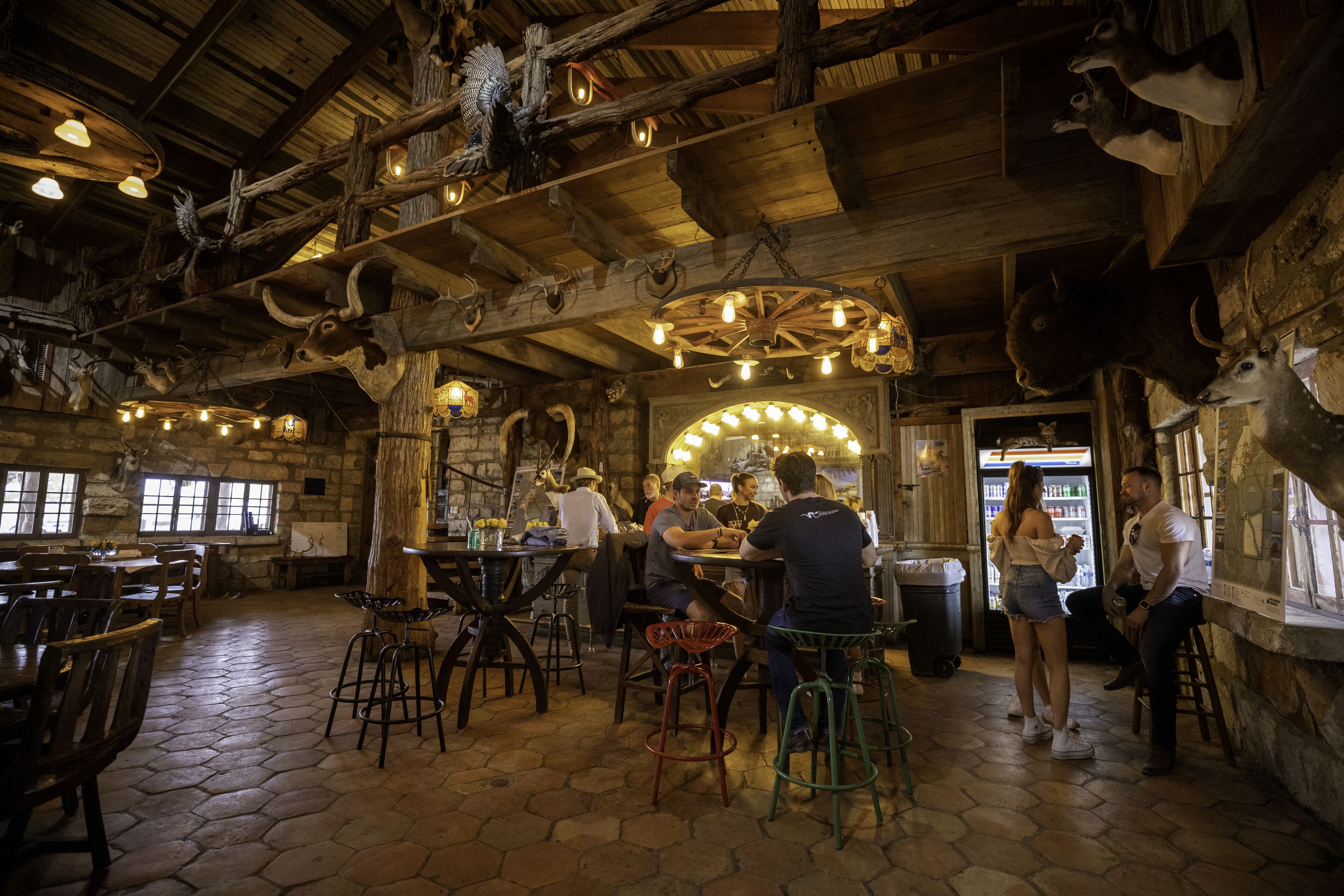 Ein rustikales Interieur mit Holzbalken, Steinwänden und einer zentralen Bar mit Hockern und Tischen.