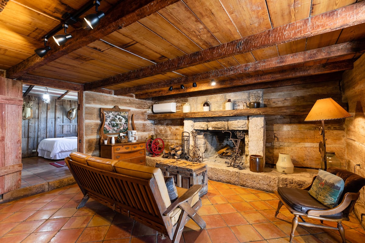 Interior rústico de cabana com teto de madeira, lareira, um banco e uma mesa de jantar.