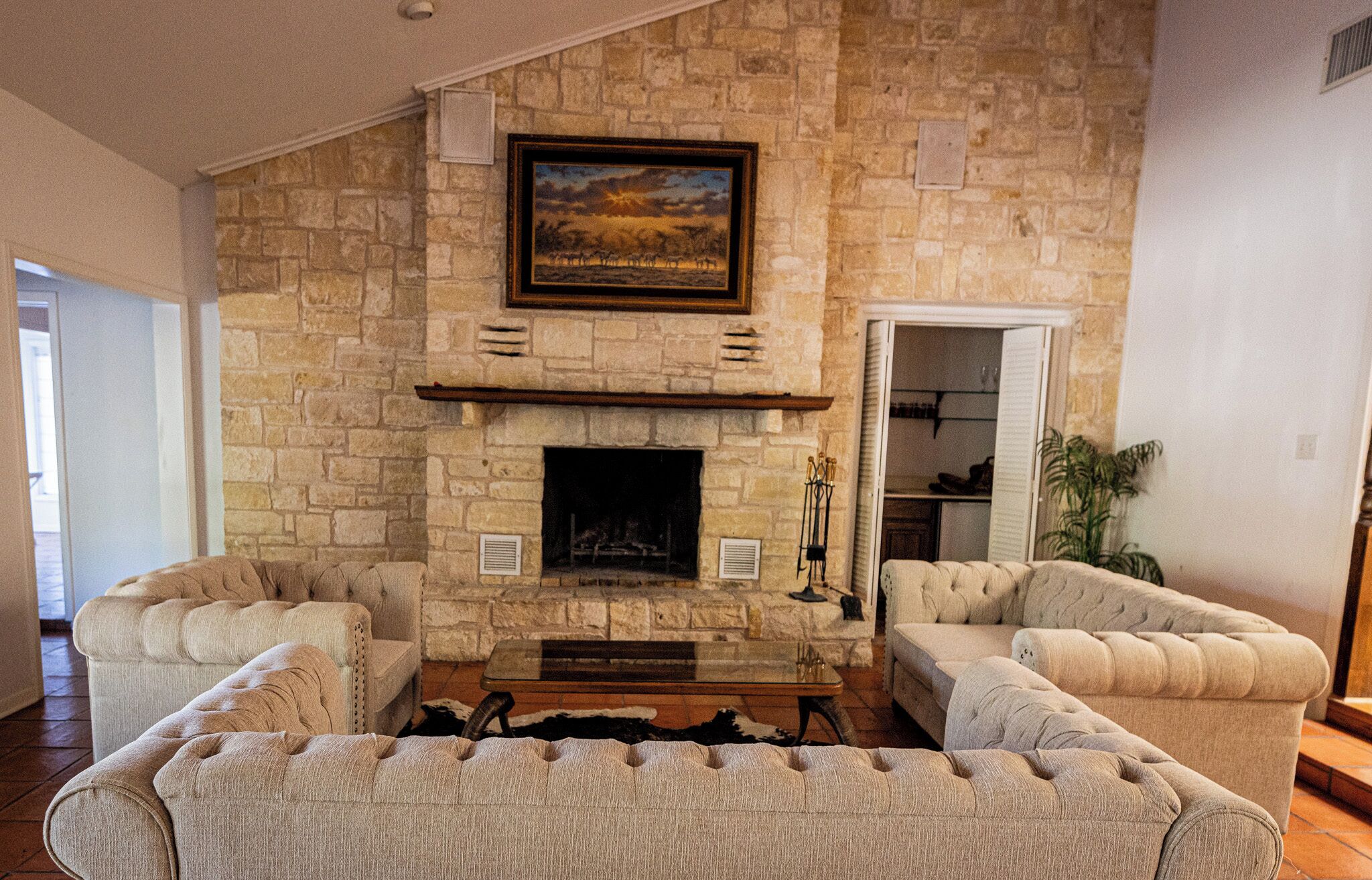 A living room with a stone fireplace, two armchairs, a coffee table, and a painting above the fireplace.