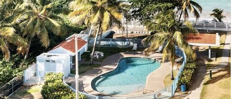 Una piscina rodeada de palmeras y un edificio blanco con techo rojo.