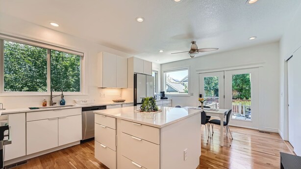 A modern kitchen with white cabinetry, a central island, and a dining area with a table and chairs. - Modern Comfort in Central Park: 4BR Home in Denver (Denver)