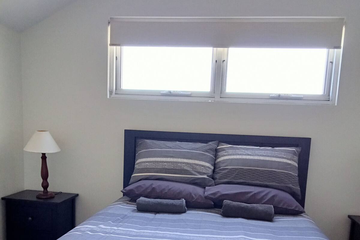 Un dormitorio con una cama, una mesita de noche, una lámpara y una ventana.