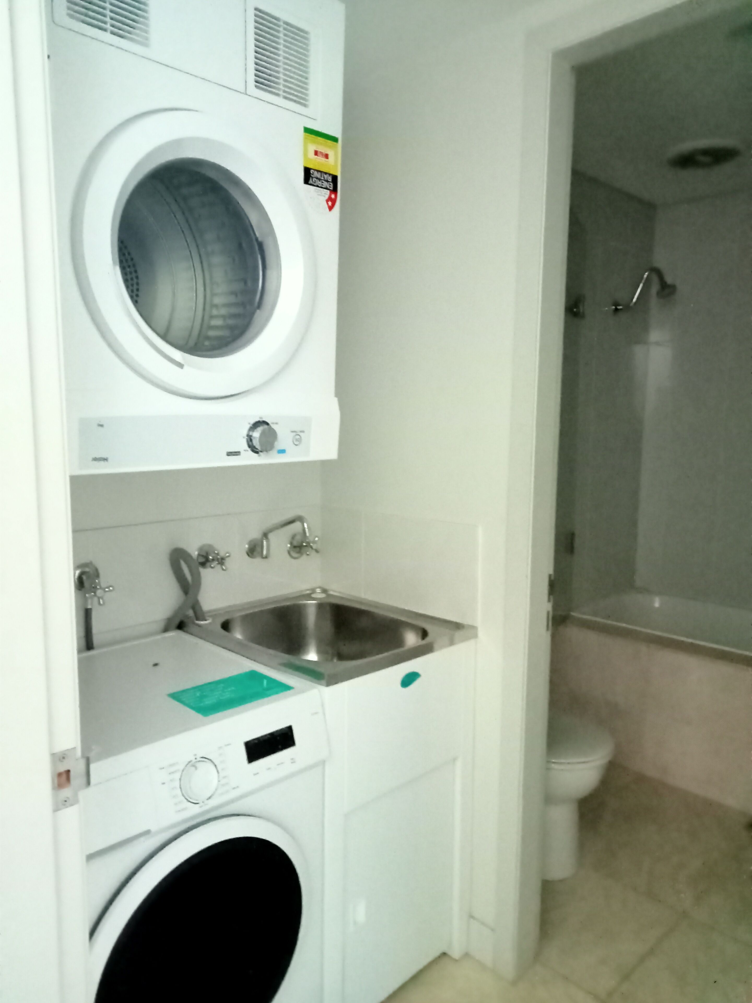 A compact laundry room with a front-loading washing machine, a sink, and a shower.