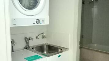 A compact laundry room with a front-loading washing machine, a sink, and a shower.