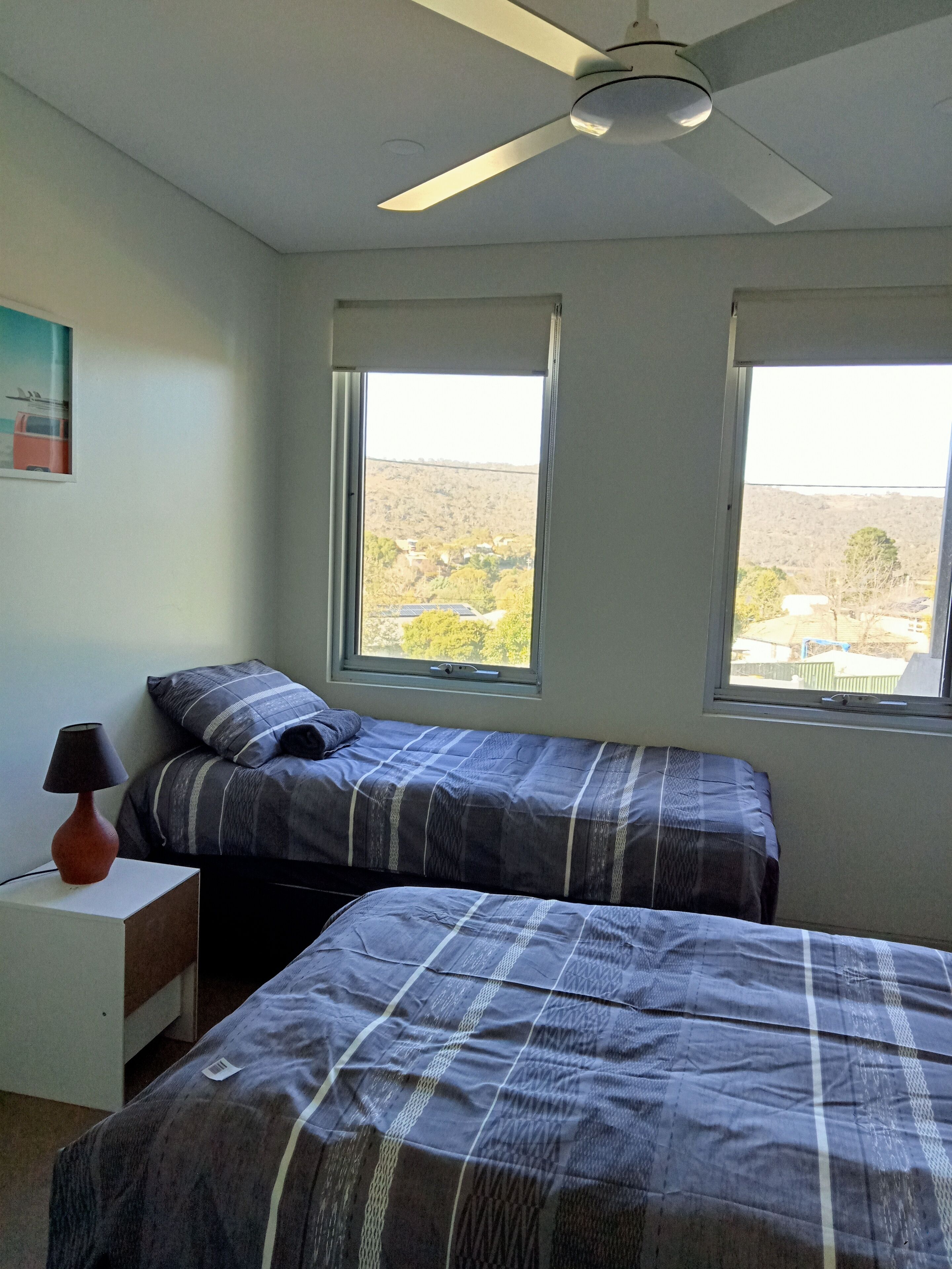 Een slaapkamer met twee bedden, een plafondventilator en ramen met uitzicht op een heuvelachtig landschap.