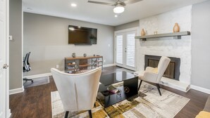 A modern living room with a fireplace, a ceiling fan, and a flat-screen TV mounted on the wall.