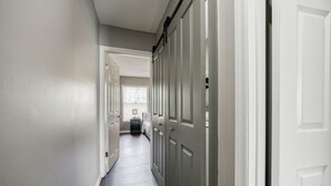 A hallway with a wooden floor, white walls, and a door on the right.