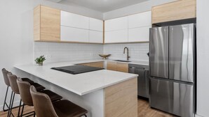 Una cocina moderna con armarios blancos, un refrigerador de acero inoxidable y una isla central con taburetes de bar.