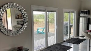 A modern living room with a large mirror, sliding glass doors leading to a patio, a ceiling light fixture, and a refrigerator.