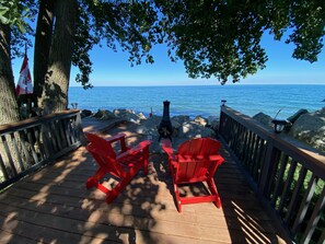 A wooden deck with red Adirondack chairs facing a rocky shoreline and the sea.