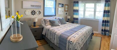 A bedroom with a bed, nightstands, a dresser, a mirror, and a window with curtains.