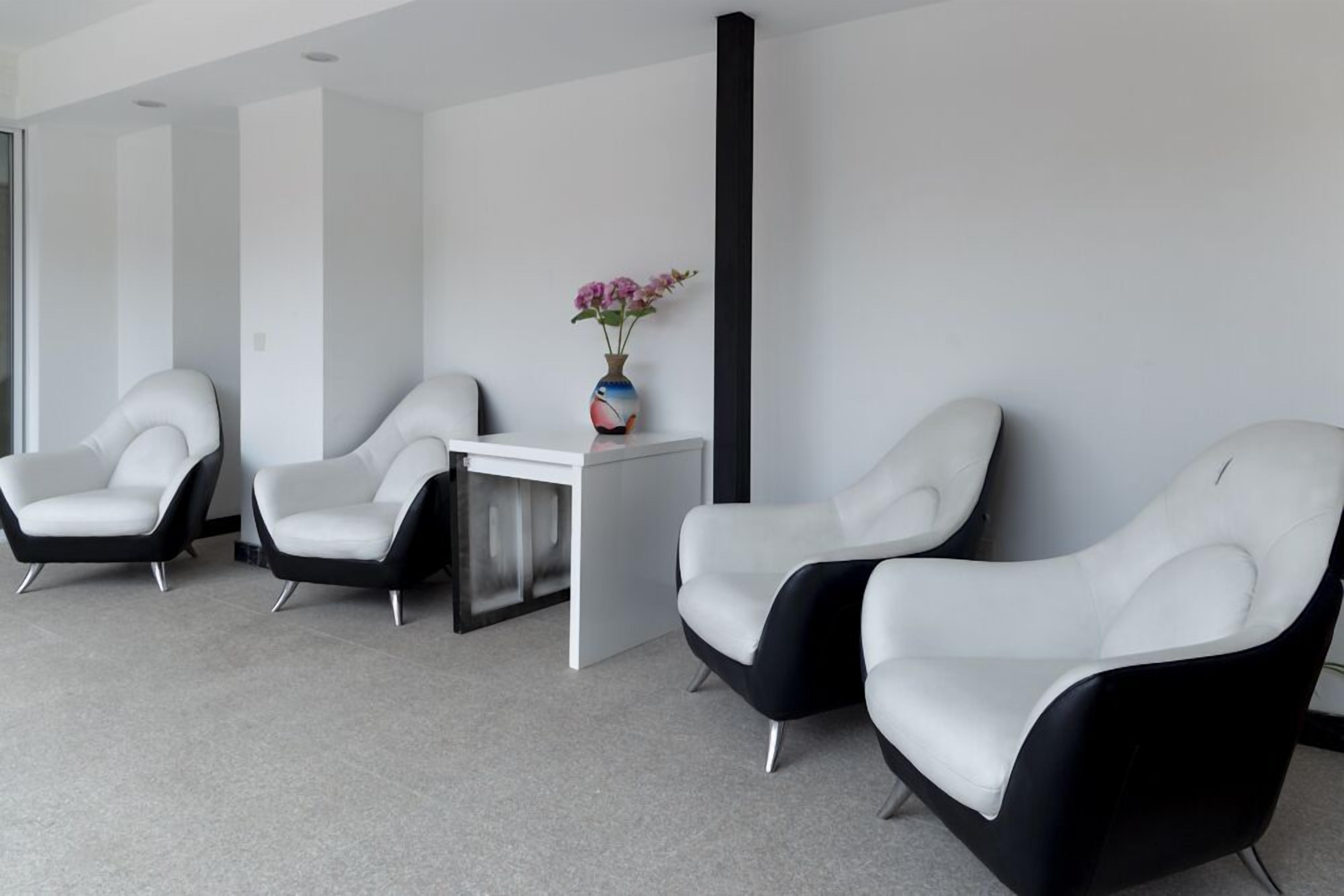 Un espace d’attente moderne avec trois fauteuils en cuir blanc et une petite table sur laquelle est posé un vase de fleurs.