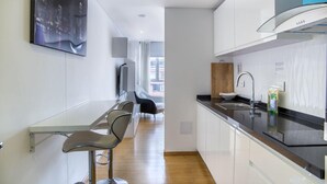 A modern kitchen with white cabinets, a black countertop, and a stainless steel sink. There is a bar area with bar stools and a large window in the background. - Apartasuite Edificio Monir (Bogotá)