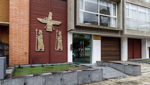 A building facade with a large red shutter, a stone relief sculpture, and a modern glass entrance. - Apartasuite Edificio Monir (Bogotá)