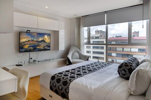 A modern hotel room with a large bed, a TV mounted on the wall, a desk, and a chair. - Apartasuite Edificio Monir (Bogotá)