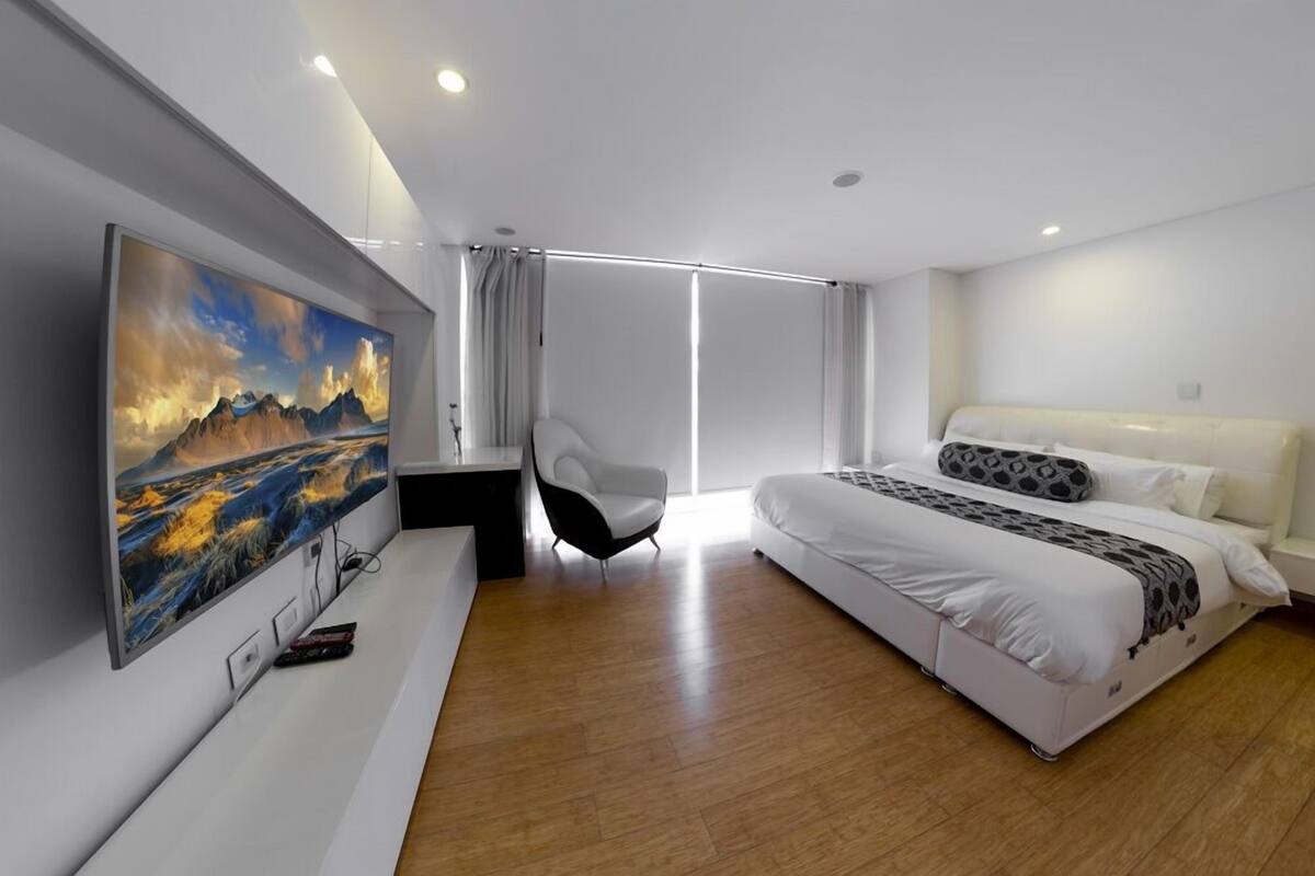A modern hotel room with a large bed, a desk, a chair, and a TV mounted on the wall.