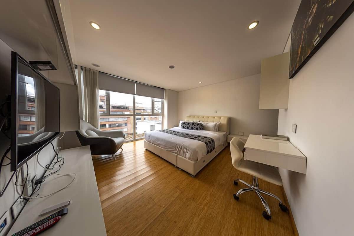 A modern hotel room with a bed, desk, chair, and TV.