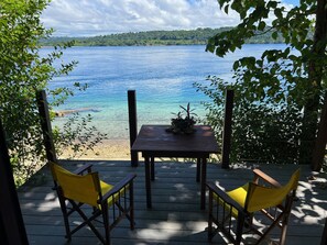 A wooden deck with two yellow chairs and a table, overlooking a clear blue lake with a forested shoreline. - Freshwater Private Resort (Aore Island)