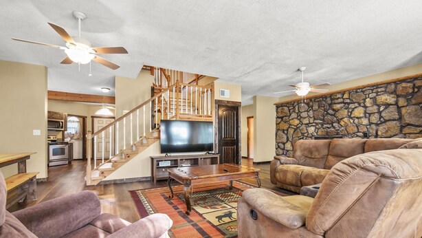 A spacious living room with a large flat-screen TV, comfortable seating, a wooden staircase, and a stone wall.
