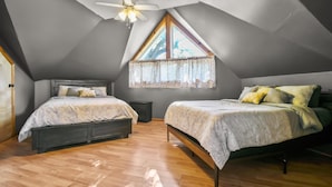 A bedroom with two beds, a ceiling fan, a window with a curtain, and a wooden floor.