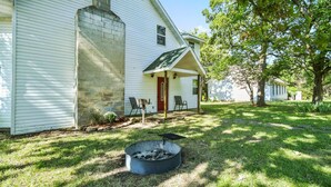 A white house with a stone chimney, a fire pit, and a covered porch with chairs.