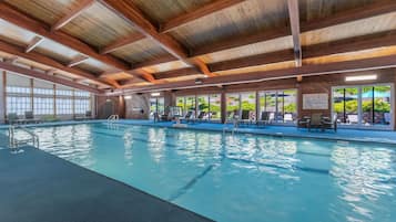 Una piscina interior con techo de madera, ventanas amplias y sillones de descanso.