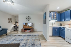 A modern living room with a flat-screen TV, a blue sofa, and a patterned rug.