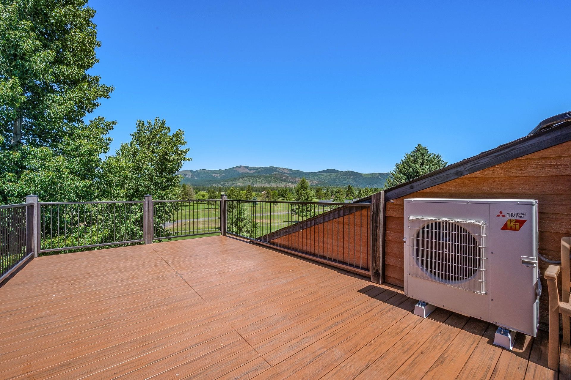 Una terraza de madera con vistas a montañas, una unidad de aire acondicionado Mitsubishi Electric y un área cercada.
