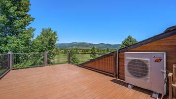 Una terraza de madera con vistas a montañas, una unidad de aire acondicionado Mitsubishi Electric y un área cercada.