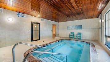 An indoor swimming pool with a wooden ceiling, a glass door, and two turquoise chairs.