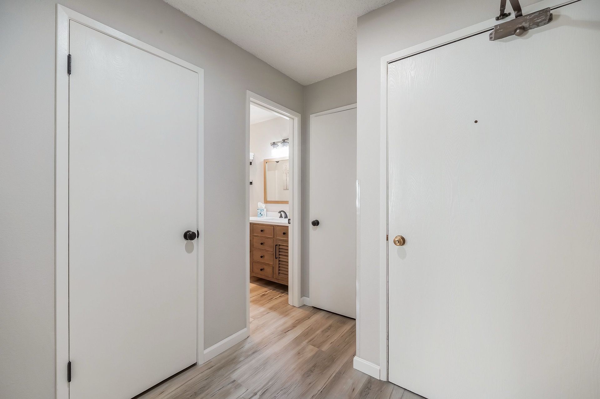 A hallway with white doors leading to a bathroom and a kitchen area.