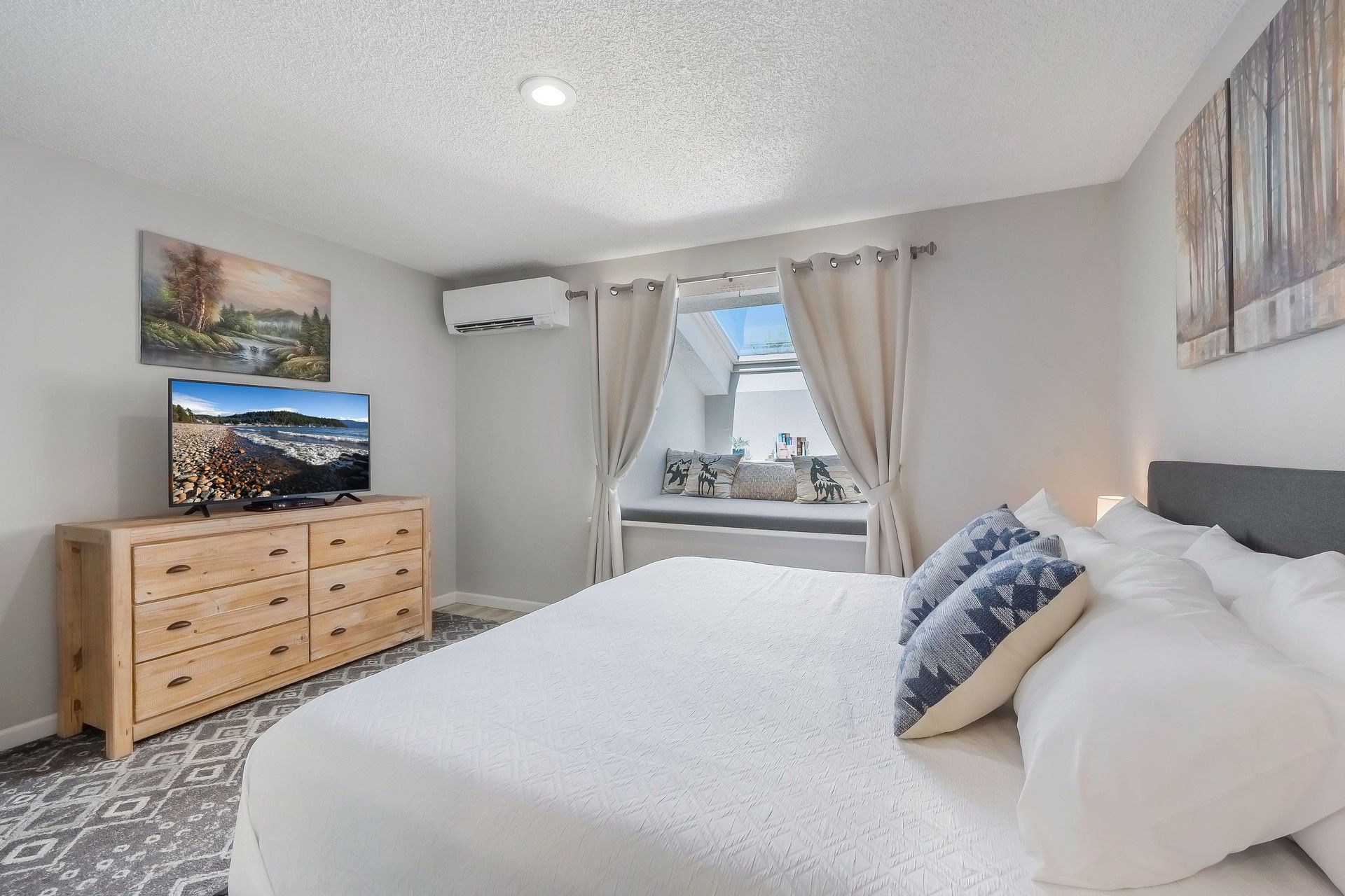 A bedroom with a bed, a dresser, a television, and a window with curtains.
