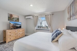 A bedroom with a bed, a dresser, a television, and a window with curtains.